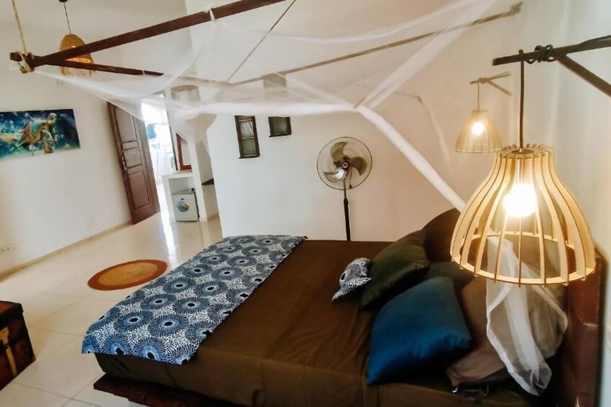 A bedroom with a bed, pillows, a hanging light fixture, a fan, and a painting on the wall.