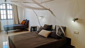 A bedroom with a bed, a chair, a small table, and a window.