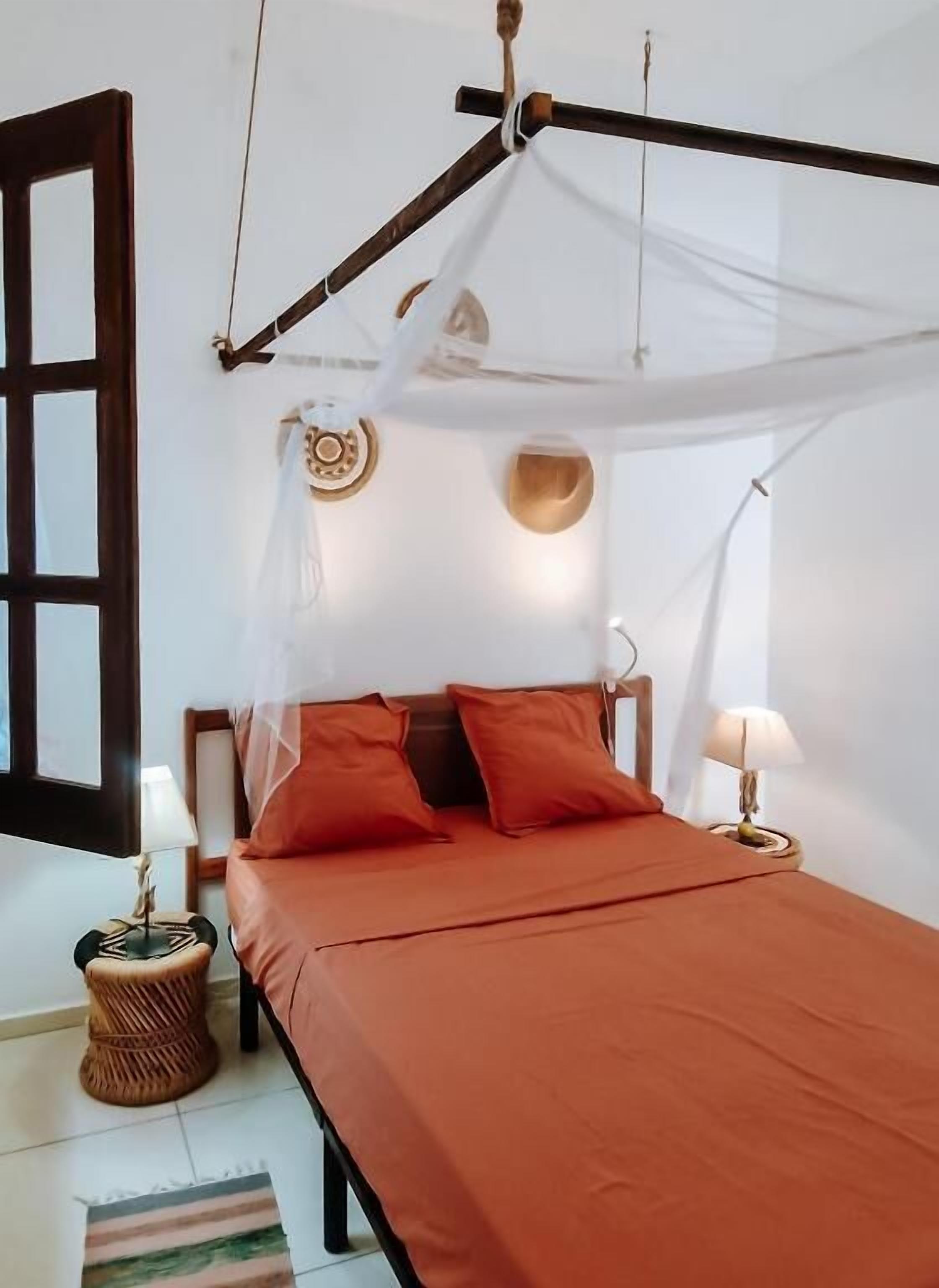 A bed with a canopy, two pillows, a bedside lamp, a decorative wall plate, and a window with a wooden frame.