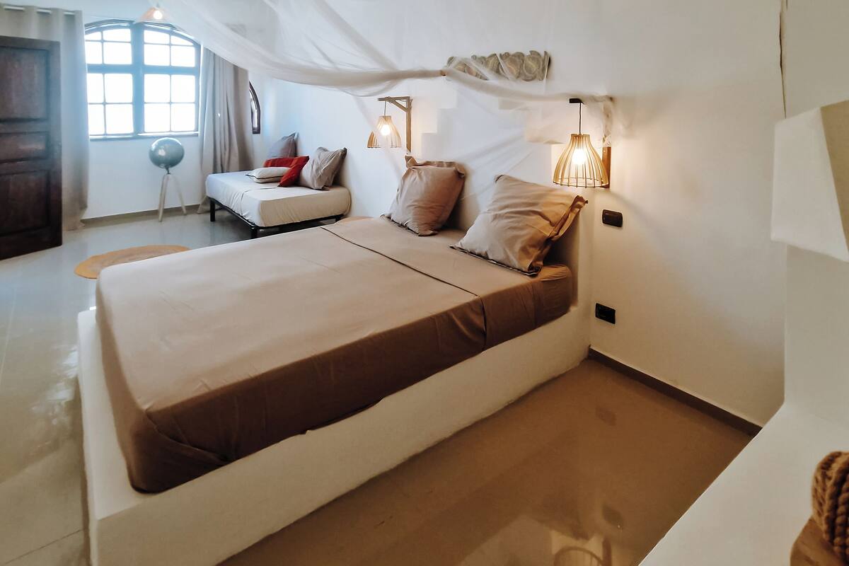 A bedroom with a large bed, bedside lamps, a window with curtains, and a wooden floor.