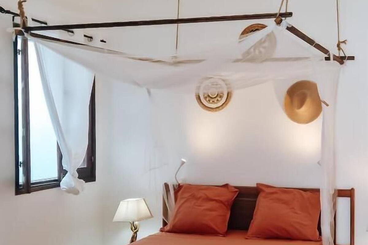 A bedroom with a bed, pillows, a lamp, and a hat hanging on the wall.