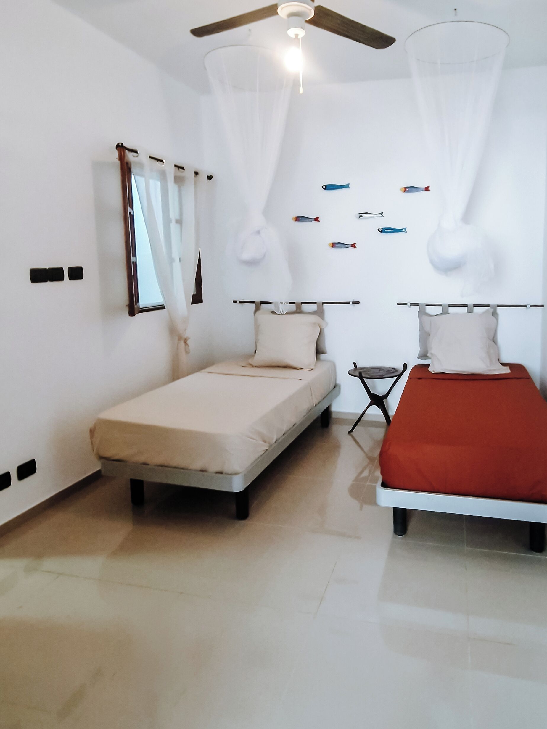A bedroom with two beds, a ceiling fan, a small table, and a wall-mounted mirror.
