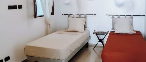 A bedroom with two beds, a ceiling fan, a small table, and a wall-mounted mirror.