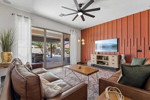 Un salon moderne avec un canapé, une table basse, un téléviseur et un ventilateur de plafond.