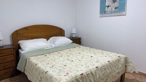A bedroom with a wooden bed, a green bedspread, a nightstand with a lamp, and a wall-mounted picture. - Caminho da Praia Apartment (Praia do Almoxarife)