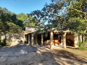 An outdoor courtyard with a building featuring columns and a covered area with firewood. - Character house, between Aix-en-Provence and the Lubéron (Saint-Cannat)