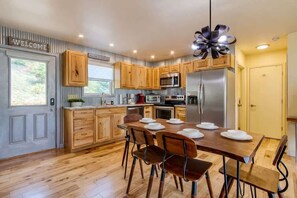 A modern kitchen with wooden cabinets, stainless steel appliances, and a dining table set for four. - Hot Tub Retreat | 1 Mile to Gatlinburg Fun (Gatlinburg)
