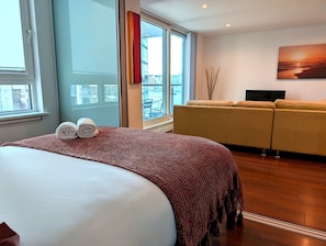 Habitación de hotel con una cama grande, un sofá, un televisor y vistas a la ciudad desde la ventana.