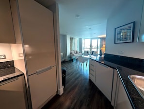 Una cocina moderna con refrigerador, un comedor con mesa y sillas, y una sala de estar con sofá y vista panorámica de la ciudad.