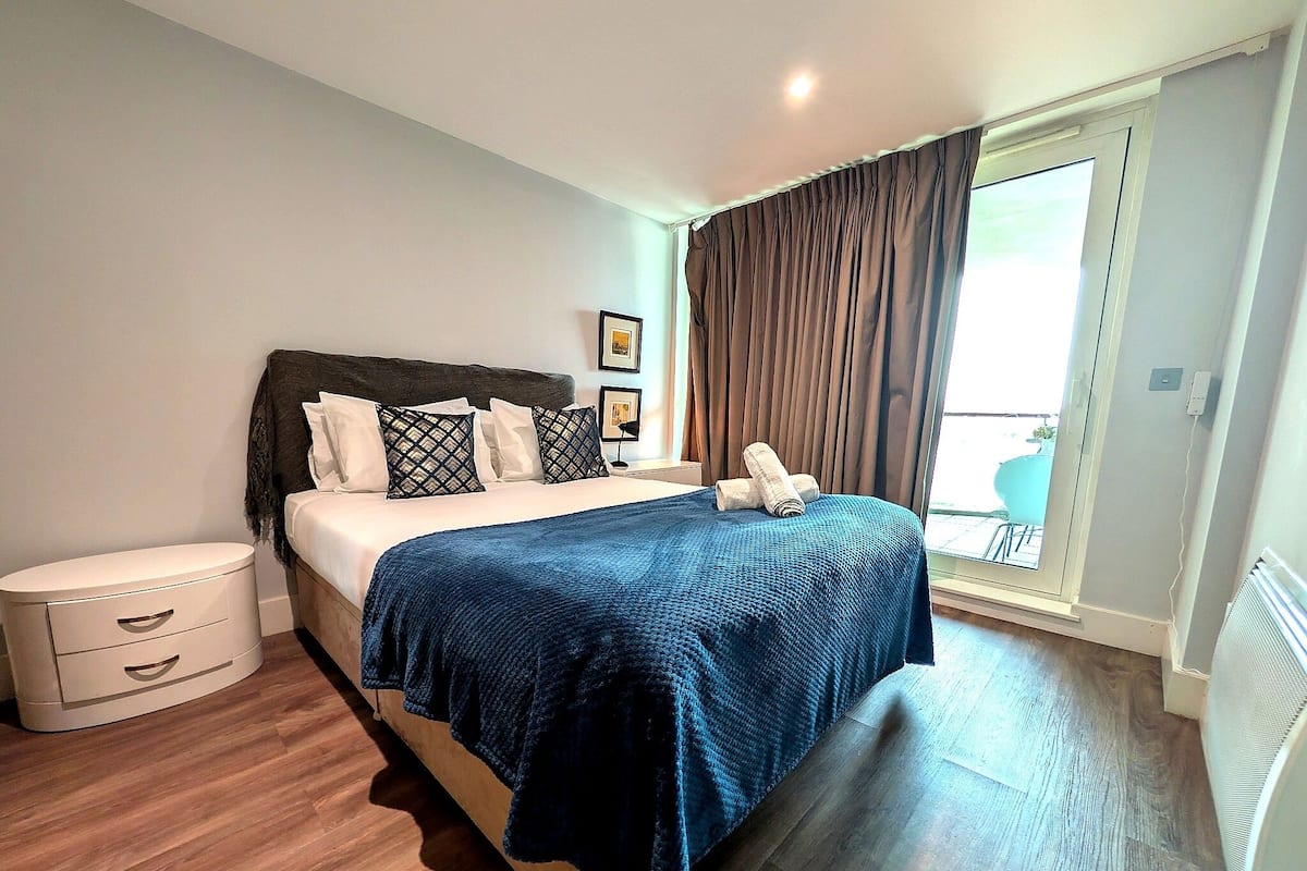 A bedroom with a bed, bedside table, and a view of the outside.
