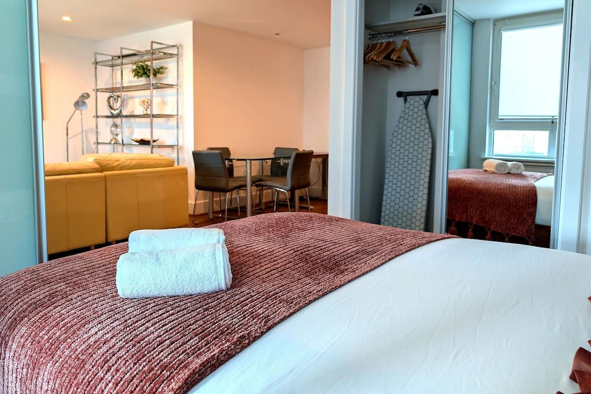 A hotel room with a bed, a sofa, a dining table with chairs, a wardrobe, and a window.