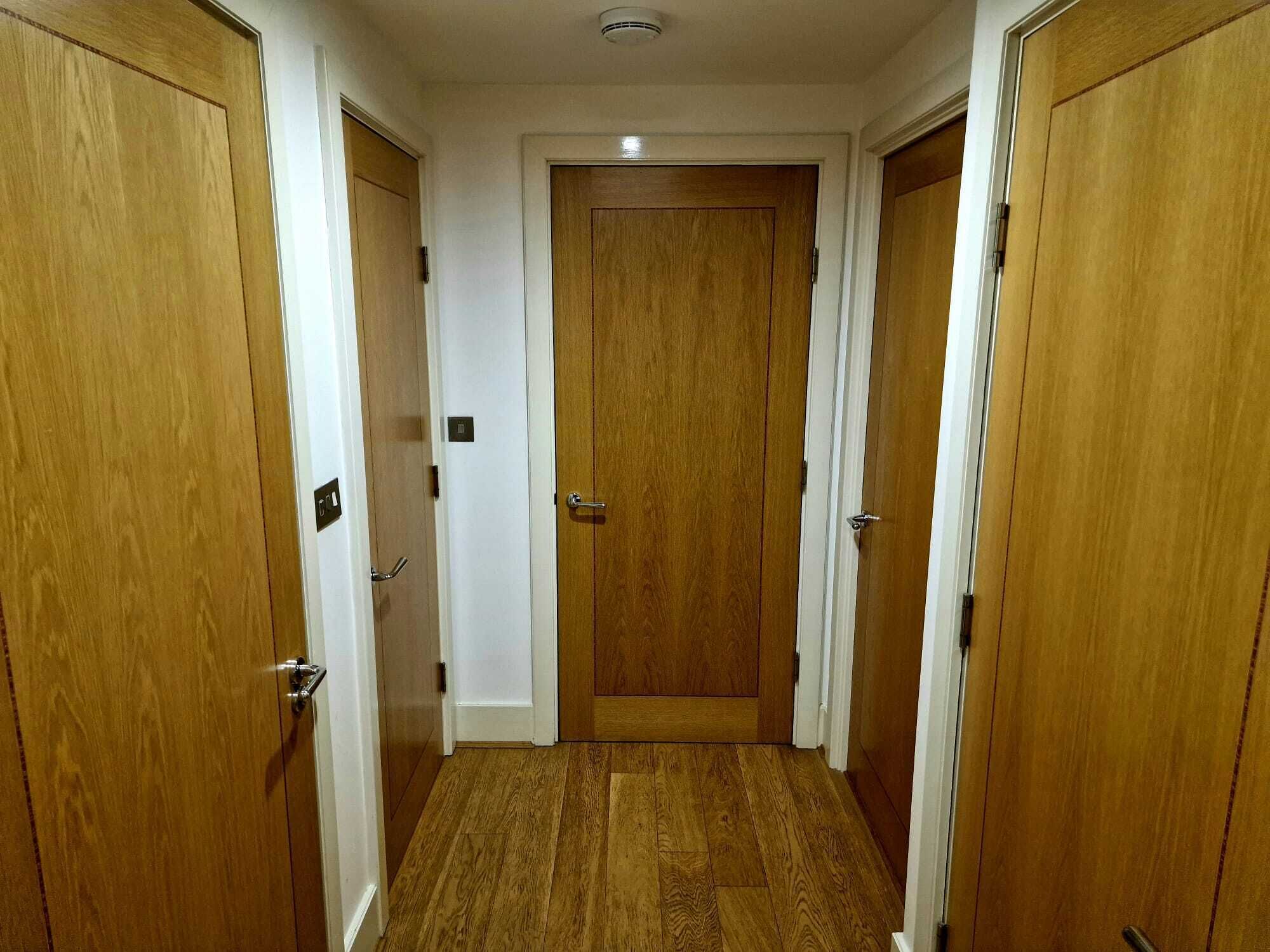 Um corredor estreito com portas de madeira em ambos os lados e uma porta no centro.