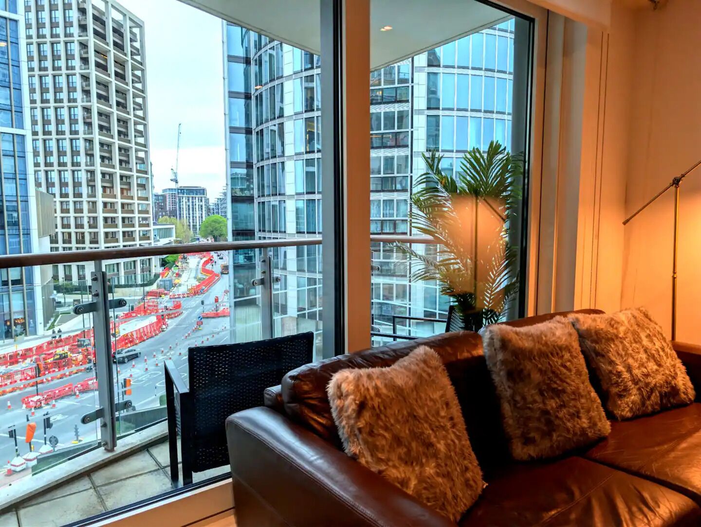 A room with a leather sofa, a large window with a view of a cityscape, and a potted plant.