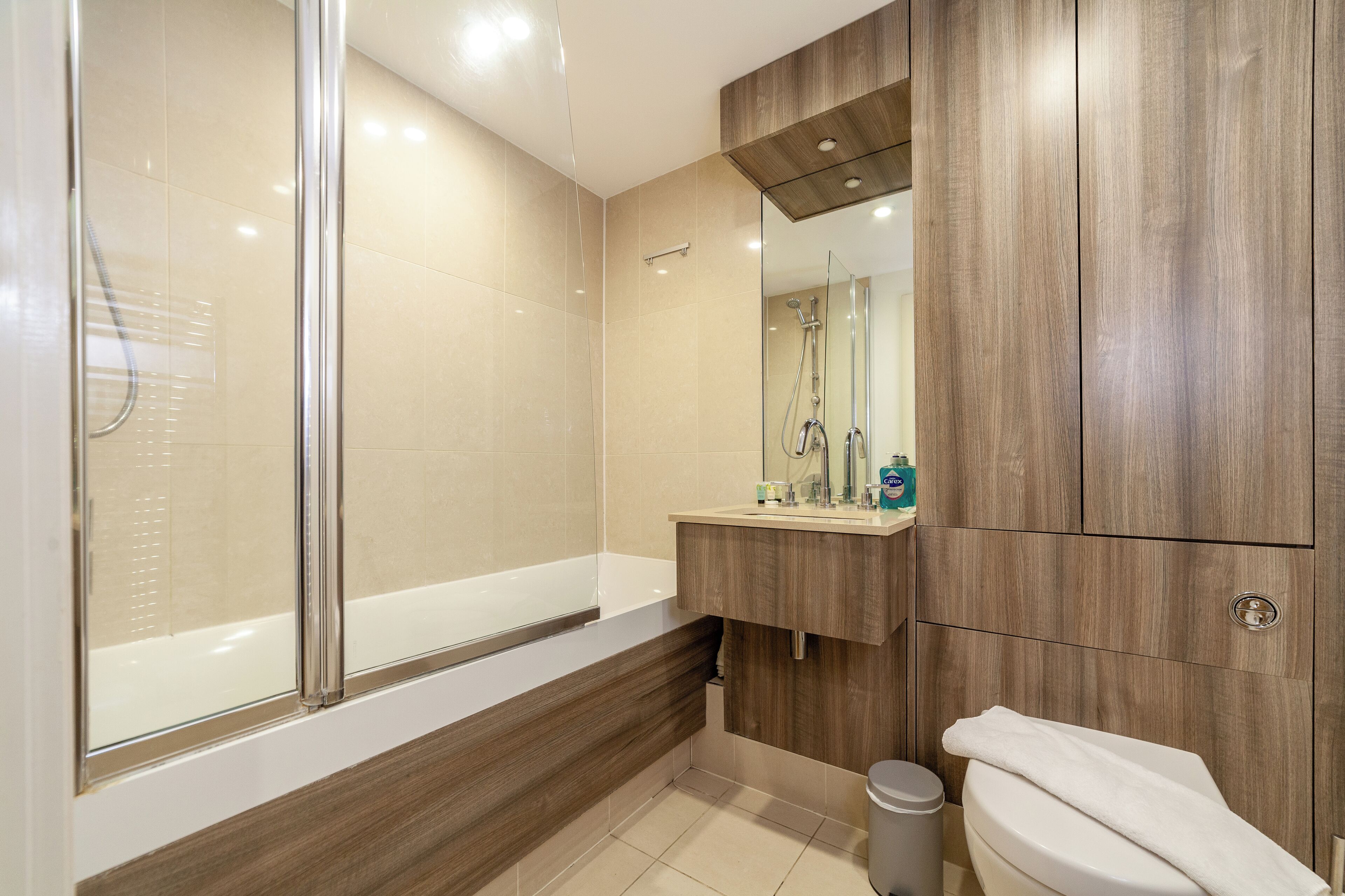 Ein modernes Badezimmer mit einer Glaskabine zur Dusche, einem Holzlagerraum und einer Toilette.