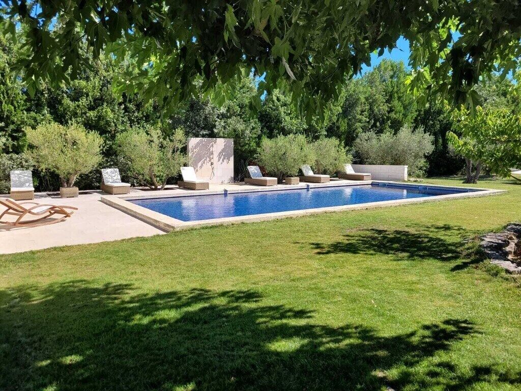 A rectangular swimming pool with a tiled edge, surrounded by a well-maintained lawn and various seating options including lounge chairs and a stone bench.