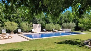 A rectangular swimming pool with a tiled edge, surrounded by a well-maintained lawn and various seating options including lounge chairs and a stone bench. - 18th century Provencal farmhouse - semi-detached - with exclusive pool area (Saint-Étienne-du-Grès)