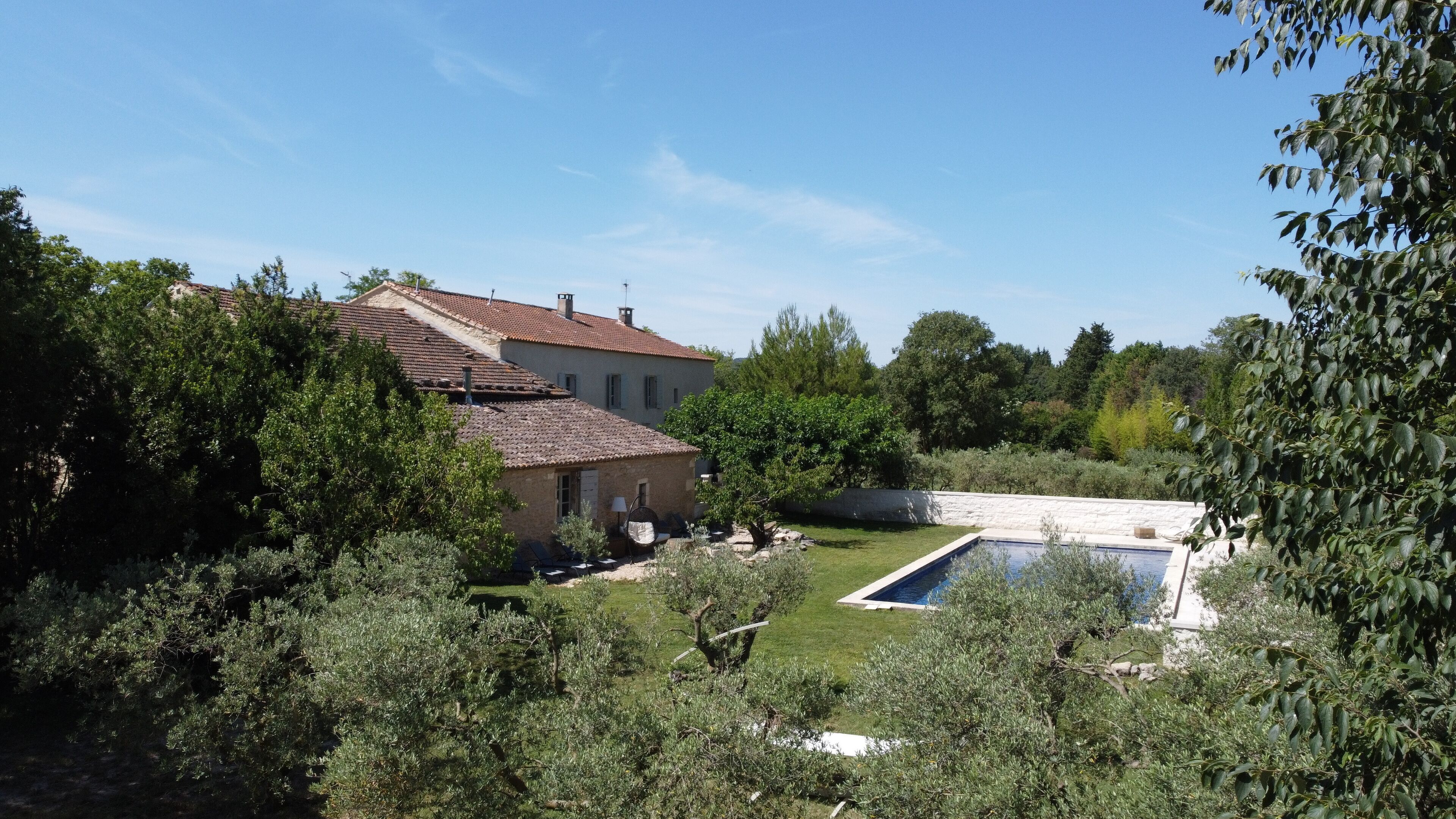 A house with a tiled roof, a swimming pool, and surrounding greenery.