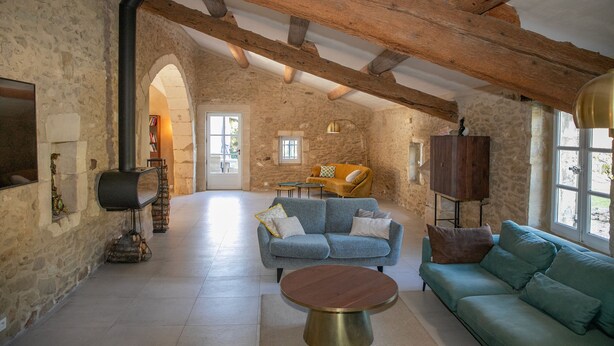 A spacious living room with stone walls, wooden beams, a blue sofa, a round coffee table, and a fireplace. - 18th century Provencal farmhouse - semi-detached - with exclusive pool area (Saint-Étienne-du-Grès)