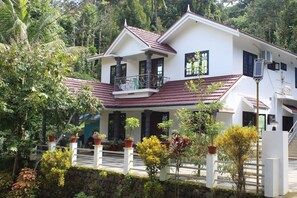 A two-story house with a balcony, surrounded by lush greenery. - Beautiful Homestay near Munnar with four attached bathrooms (Anaviratty)
