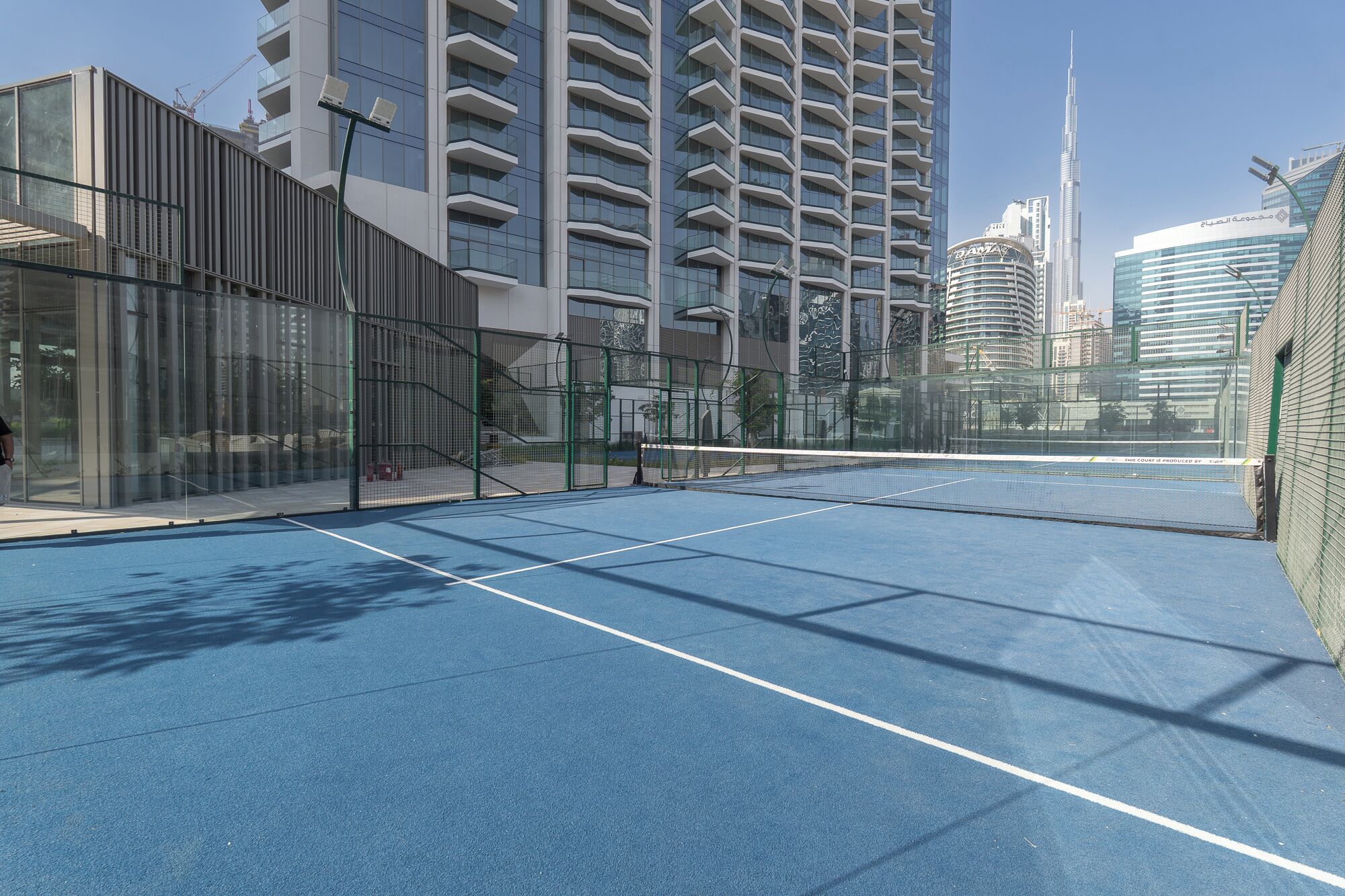An outdoor tennis court with a clear view of surrounding high-rise buildings.
