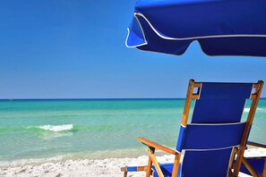 Een strandstoel en parasol op een zanderig strand met helder turquoise water en een heldere lucht.