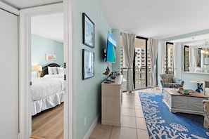 A hotel room with a bed, a desk, a chair, a large mirror, and a view of buildings outside. - 🏖️FREE Beach Service-Pools + Hot Tub | Gulf Views | Surfside Resort #410🌊 (Miramar Beach)