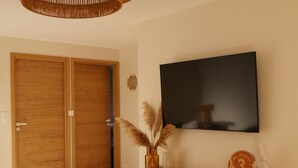 A modern living room with a large flat-screen TV mounted on the wall, wooden double doors, a wooden console table with decorative items, and a woven floor rug. - New apartment "La vieille maison", near Serre Chevalier (Villar-Saint-Pancrace)