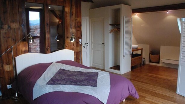A bedroom with a bed, wooden walls, a white door, and a hanging light fixture.