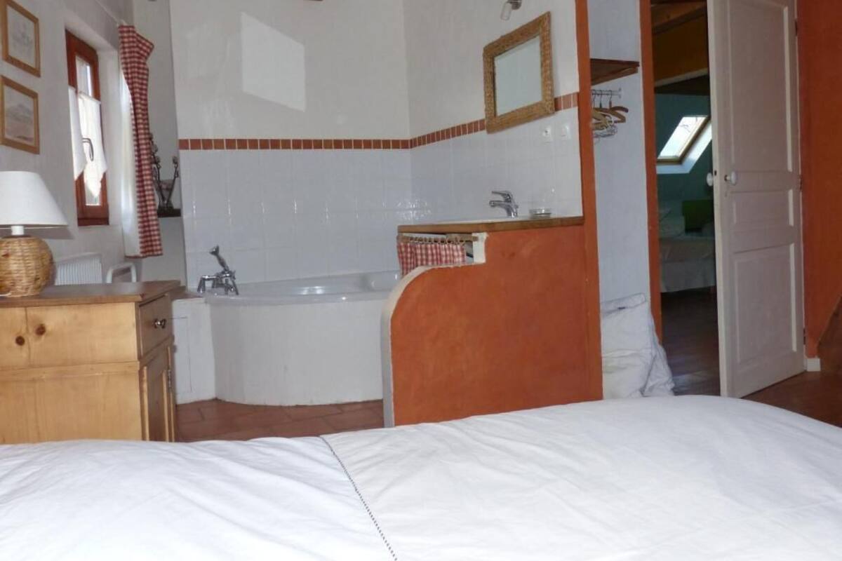 Une chambre avec un grand lit, une commode en bois, une salle de bain avec une baignoire et un miroir.