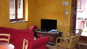 A living room with a red sofa, wooden chairs, a TV, and a brick floor.