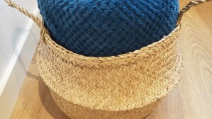 Un cesto intrecciato con un cuscino a forma di cuore blu su un pavimento di legno.