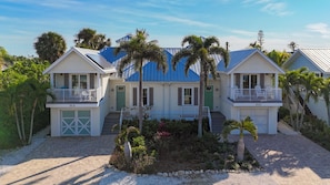 A two-story beachfront property with a blue roof, white exterior, and a small garden with palm trees. - Island Escape- 4 bedrooms with private pool and spa!! (Holmes Beach)