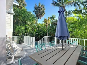 Een houten terras met een tafel en stoelen, omringd door een witte reling, en palmbomen op de achtergrond.