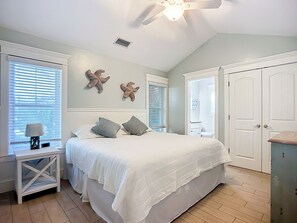 Een slaapkamer met een bed, nachtkastjes, een plafondventilator en decoratie met zeesterren.