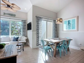 Een moderne woonkamer met een bank, een eettafel met stoelen, een plafondventilator en een groot raam met behang.