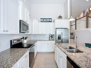 A modern kitchen with white cabinets, granite countertops, stainless steel appliances, and a sign that says "BEACH". - Island Escape- 4 bedrooms with private pool and spa!! (Holmes Beach)