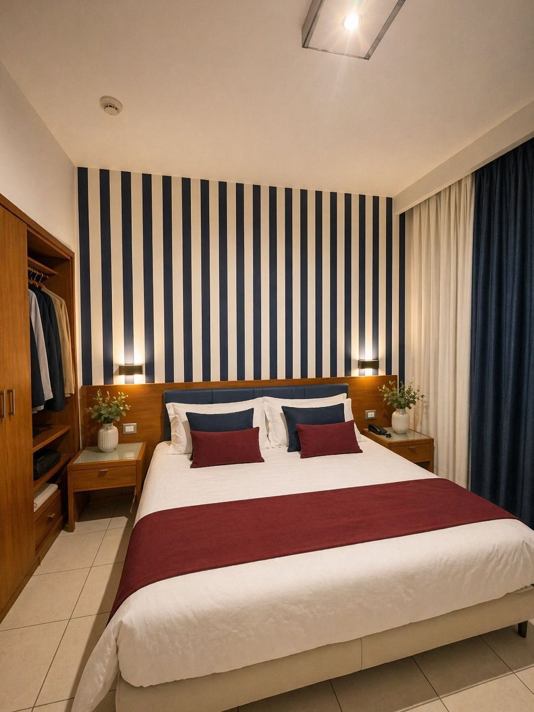 Habitación de hotel con una cama grande, un armario, una mesita de noche con lámpara y un pequeño escritorio con teléfono.