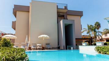 Un hotel moderno con piscina, tumbonas y sombrillas.
