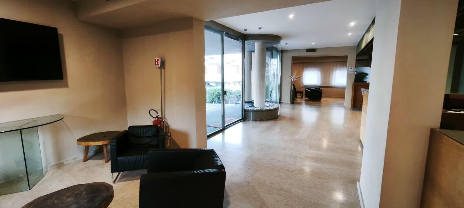 Una hall d'albergo moderna con un divisorio in vetro, una televisione a schermo piatto, un tavolino rotondo e un divano in pelle nera.