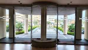 A hotel lobby with a glass entrance, a central column, and a view of the street outside. - Hotel La Costiera (Giugliano in Campania)