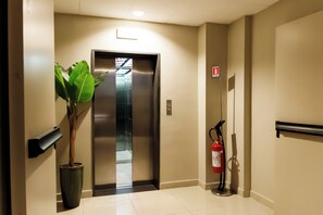 A hallway with a potted plant, an elevator, and a fire extinguisher. - Hotel La Costiera (Giugliano in Campania)