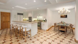 A modern kitchen with white cabinetry, a central island with bar stools, and a dining area with a round table and chairs.