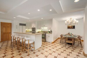 Une cuisine moderne avec des meubles blancs, un îlot central doté de tabourets, et un coin repas avec une table ronde et des chaises.