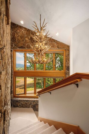 A staircase with a wooden handrail leading to a room with a stone wall and a large window.