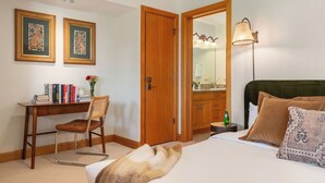 A hotel room with a bed, a desk with a chair, a wardrobe, a mirror, and a lamp.