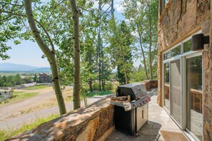 Un área de parrilla al aire libre con muro de piedra y vista a un paisaje montañoso.