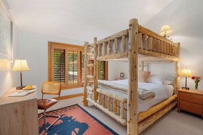 Una cama con dosel de madera, un mesita de noche a juego y una lámpara, un escritorio con una silla, y una ventana con persianas.