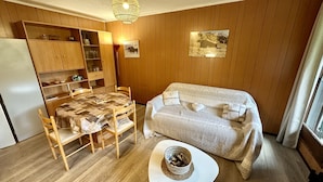 Una habitación acogedora con pared de madera, una mesa de comedor con sillas, un sofá y una pequeña mesa blanca con una cesta.