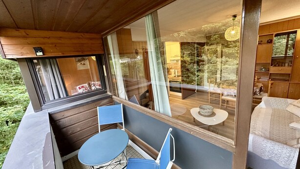 Un balcón con mesa y sillas, vista a una cocina y techo de madera.