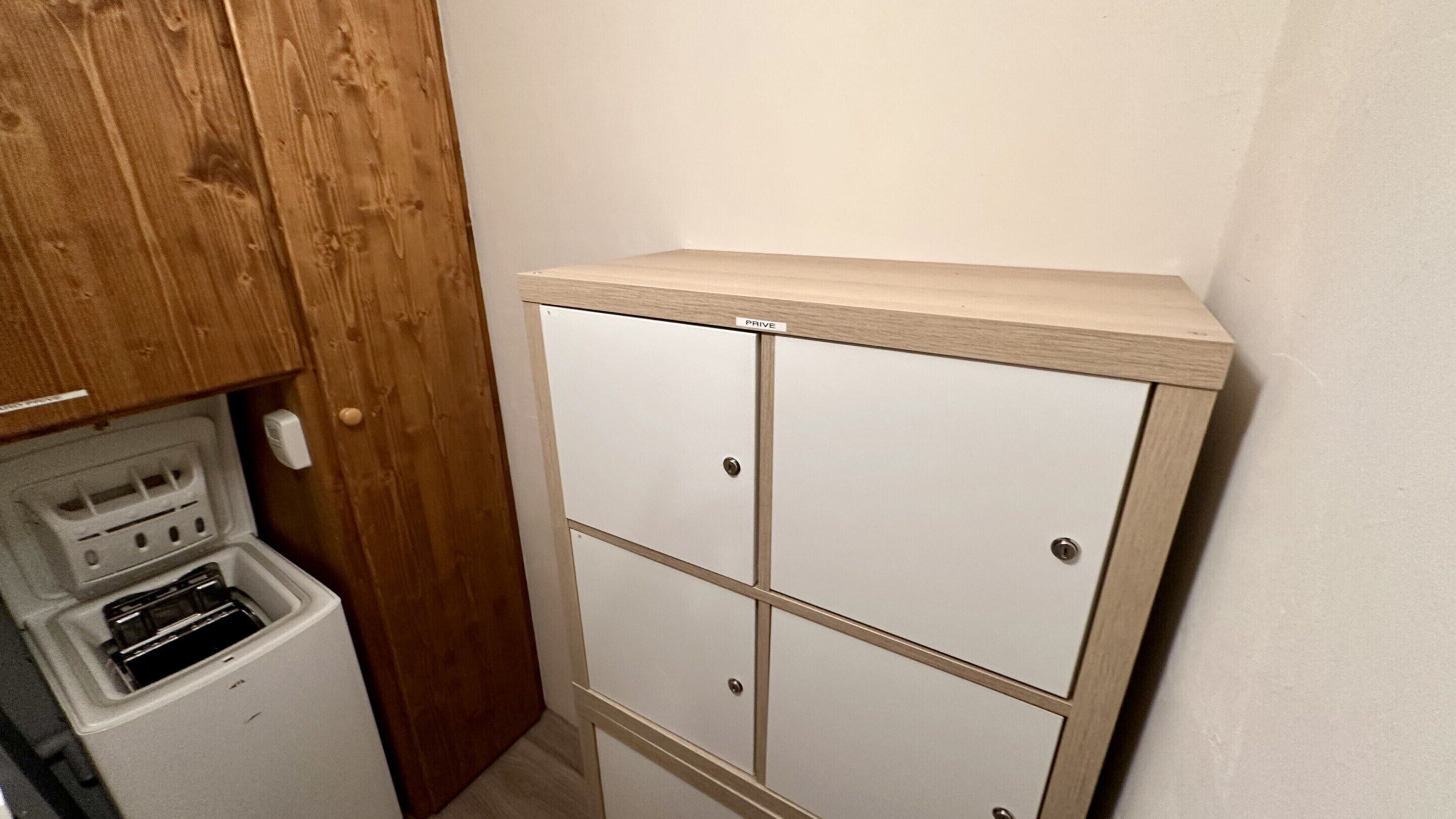A compact kitchenette with a built-in stove, a small refrigerator, and a wooden cabinet above a set of white storage units.